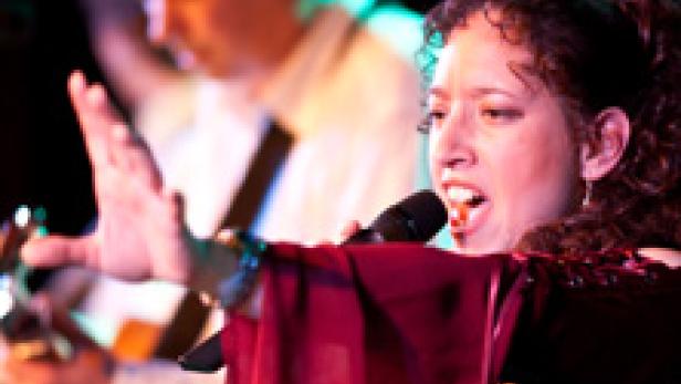 Eine Sängerin tritt mit einem Mikrofon vor einem Gitarristen auf.