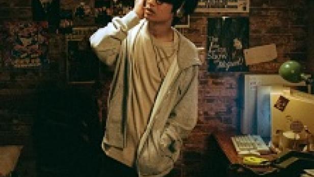 Ein junger Mann mit Brille steht in einem Zimmer mit vielen Postern an der Wand.