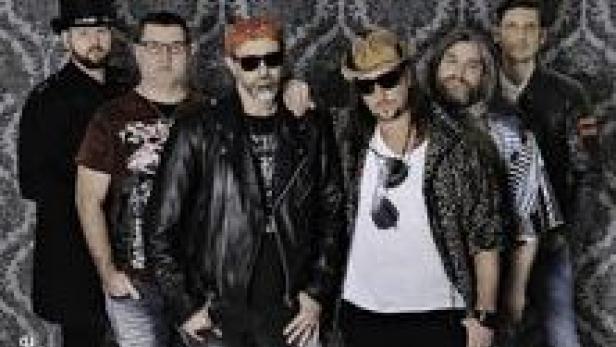 Eine Band posiert vor einer gemusterten Wand für ein Gruppenfoto.