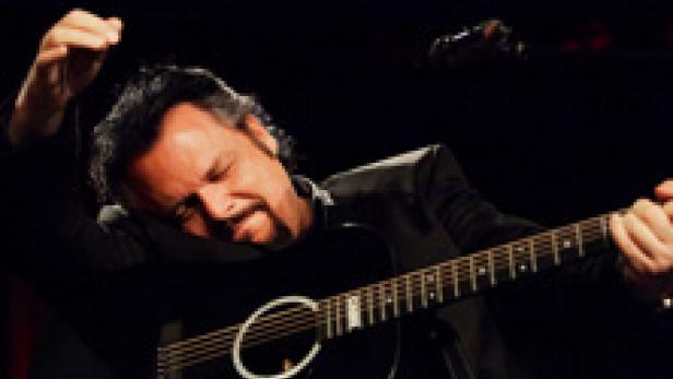 Ein Mann mit Gitarre auf einer Bühne im dunklen Licht.