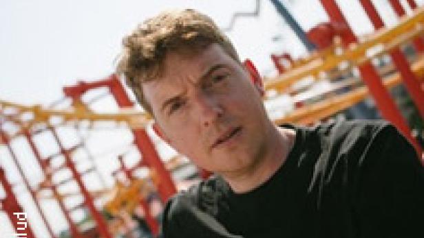 Ein Mann mit blonden Haaren vor einer Achterbahn.