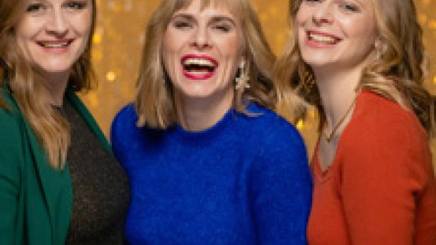 Drei Frauen stehen vor einem goldenen Hintergrund und lachen.