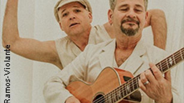 Zwei Männer posieren, einer spielt Gitarre, der andere hebt die Hand.