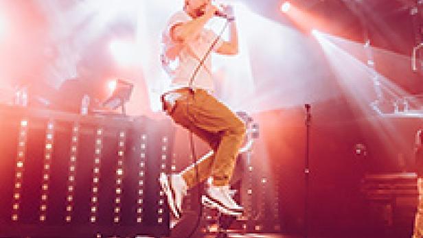 Ein Sänger springt mit einem Mikrofon in der Hand auf einer Bühne.