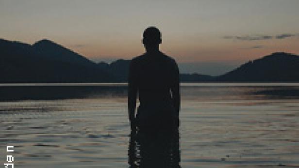 Eine Person steht im Wasser vor einer Bergkulisse im Abendlicht.