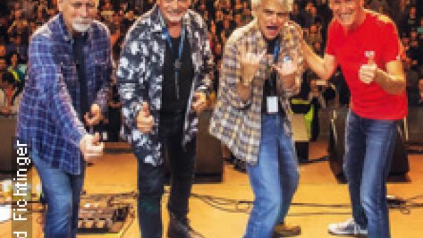 Eine Band posiert auf einer Bühne vor Publikum.