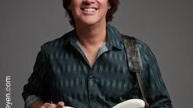 Carl Verheyen hält eine weiße E-Gitarre und lächelt.
