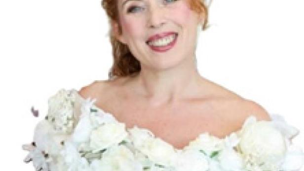 Eine lächelnde Frau mit roten Haaren trägt ein weißes Kleid mit Blumen.