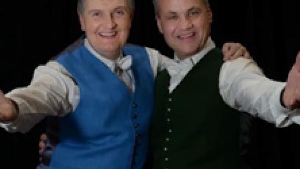 Zwei Männer in Westen lächeln und strecken die Arme aus.