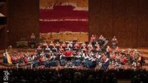 Ein großes Orchester spielt auf einer Bühne vor einem Publikum.