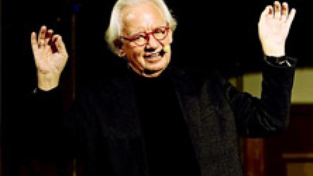 Ein älterer Mann mit Brille gestikuliert mit erhobenen Händen.