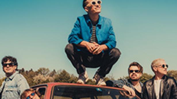 Die Band Giant Rooks posiert auf und an einem roten Auto vor blauem Himmel.