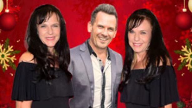 Ein Mann steht zwischen zwei Frauen vor einem weihnachtlichen Hintergrund.