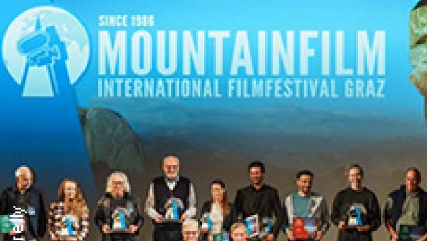 Eine Gruppe von Menschen steht auf einer Bühne vor dem Mountainfilm International Filmfestival Graz Logo.