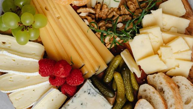 Eine Platte mit verschiedenen Käsesorten, Gemüse, Obst und Brot.