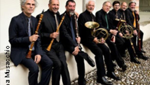 Eine Gruppe von acht Musikern sitzt mit ihren Instrumenten auf einer Mauer.