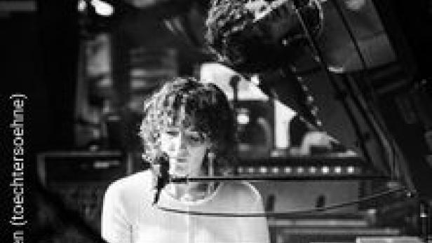 Eine Frau mit lockigem Haar spielt Klavier vor einem Mischpult.