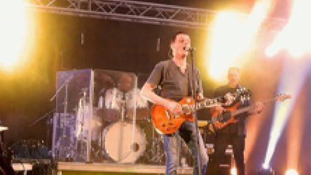 Ein Gitarrist steht auf einer Bühne während eines Konzerts.