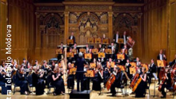 Ein Orchester spielt in einem reich verzierten Konzertsaal.