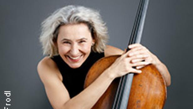 Eine lächelnde Frau mit grauem Haar umarmt ein Cello.