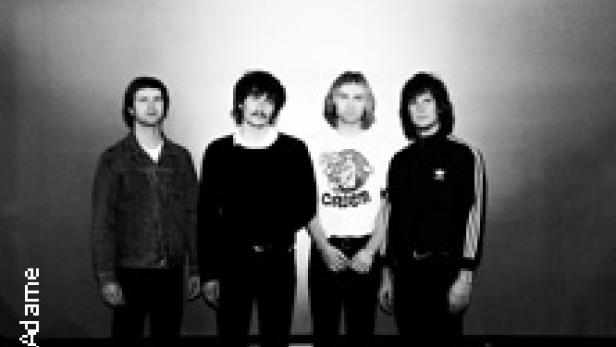 Die Band The Motors posiert vor einer Wand.