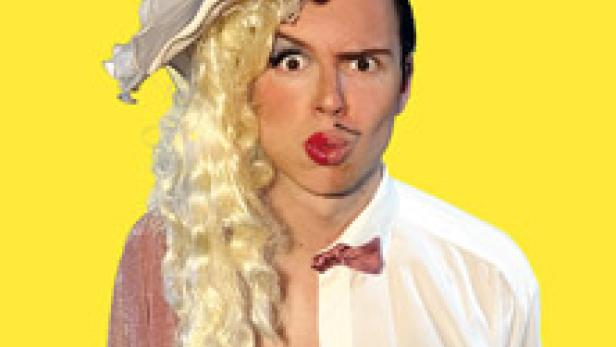 Ein Mann mit Make-up und einer Perücke, zur Hälfte in Damen- und zur Hälfte in Herrenkleidung gekleidet.