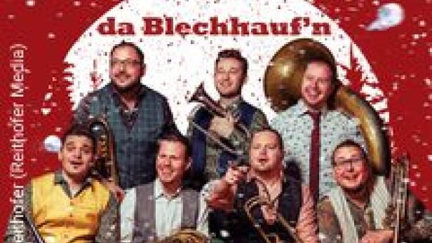 Die Blaskapelle „da Blechhauf’n“ posiert vor einem weihnachtlichen Hintergrund.