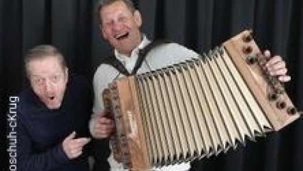 Zwei Männer posieren mit einer Steirischen Harmonika vor einem schwarzen Vorhang.