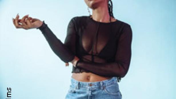 Eine junge Frau mit dunkler Haut und geflochtenen Zöpfen posiert vor einem hellblauen Hintergrund.