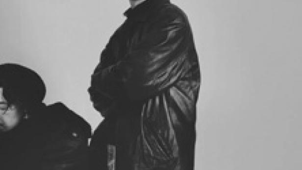 Ein Mann mit verschränkten Armen in einer schwarzen Jacke vor einem hellen Hintergrund.