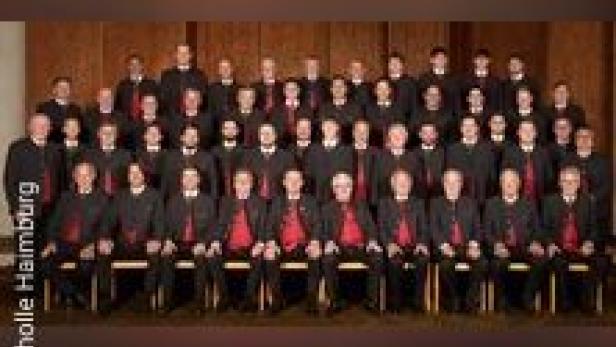 Ein großer Männerchor in schwarzer Kleidung mit roten Akzenten sitzt für ein Gruppenfoto.
