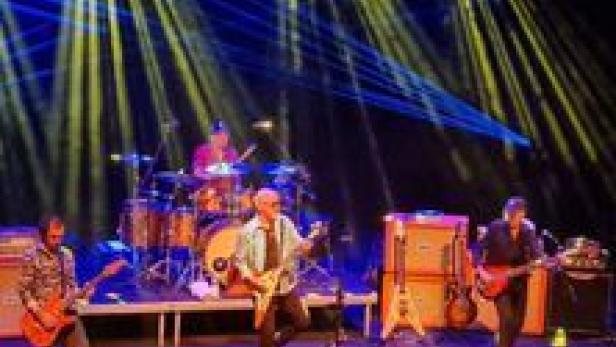 Eine Band spielt auf einer Bühne mit gelber und blauer Beleuchtung.