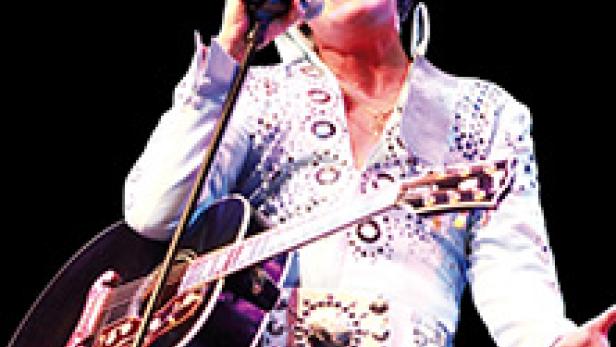 Ein Elvis-Presley-Imitator singt mit Gitarre auf einer Bühne.