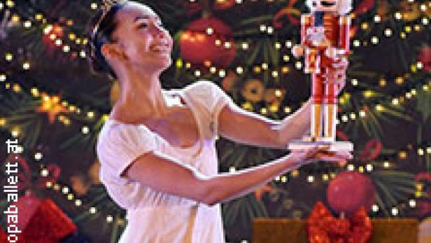 Eine Ballerina hält einen Nussknacker vor einem Weihnachtsbaum.