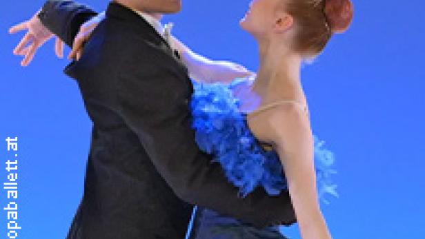 Ein Tänzerpaar in Kostümen tanzt vor einem blauen Hintergrund.