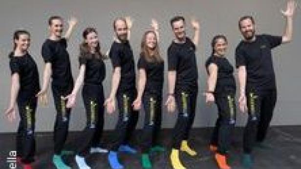 Eine Gruppe von acht Personen posiert in schwarzen Jogginghosen und T-Shirts mit bunten Socken.