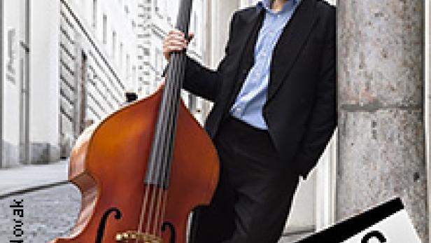 Ein Mann mit Kontrabass lehnt an einer Säule in einer Stadt.