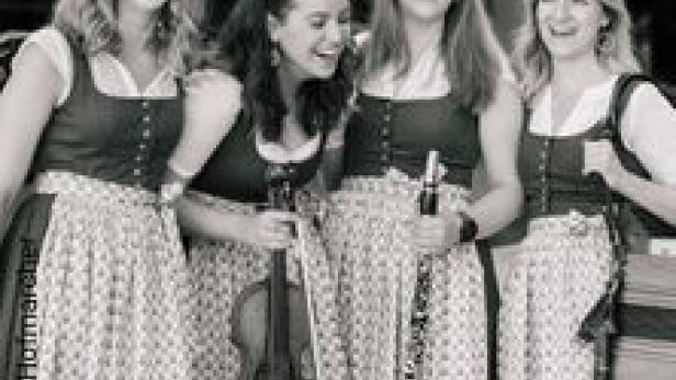Vier Frauen in Dirndln lachen und halten Musikinstrumente.