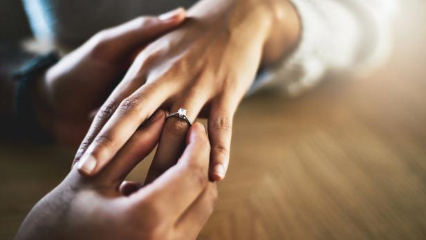 Mann steckt Ring an den Ringfinger einer Frau