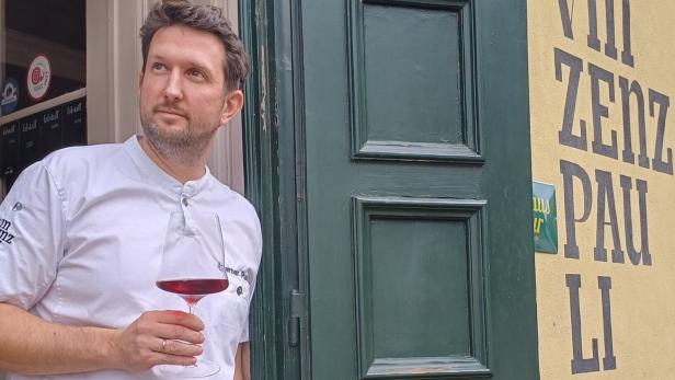 Koch Werner Punz steht vor seinem Wirtshaus „Vinzenz Pauli“ mit einem Glas Rotwein in der Hand.