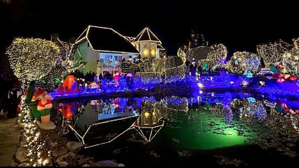 Ein festlich geschmücktes Haus mit bunten Lichtern und Dekorationen spiegelt sich in einem ruhigen Teich wider.