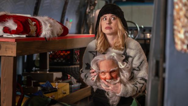 Frau in geöffnetem Laderaum eines Transporters, die eine Santa-Maske in den Händen hält