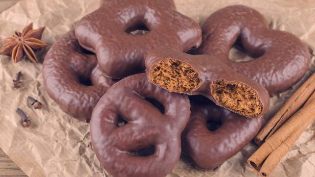 Mehrere mit Schokolade überzogene Lebkuchen in verschiedenen Formen liegen auf braunem Papier, daneben Zimtstangen und Sternanis.