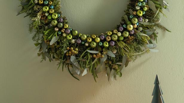 Dekorative Girlande: Tannenzweige werden mit glänzenden Kugeln in Grüntönen kombiniert, das ganze auf einem stabilen Ast befestigt. 