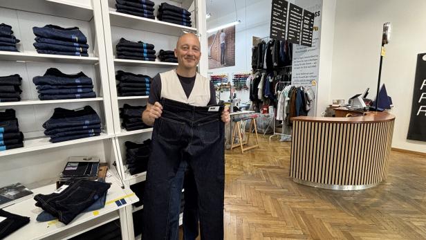 Mann in Jeansladen hält eine sehr große dunkle Jeans vor sich.