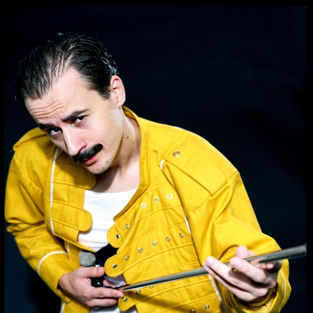 Ein Mann im Freddie-Mercury-Kostüm posiert mit einem Mikrofonständer.