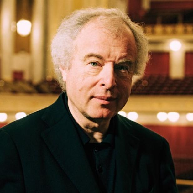 Ein Porträt von Sir András Schiff vor dem Hintergrund eines Konzertsaals.