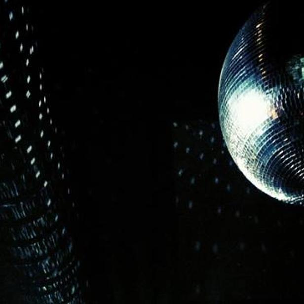 Eine glitzernde Discokugel wirft Lichtpunkte in einen dunklen Raum.