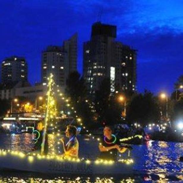 Ein mit Lichtern geschmücktes Boot fährt auf einem Fluss in Wien bei Nacht.