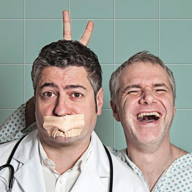 Ein Arzt mit Klebeband über dem Mund und ein lachender Patient im Hintergrund.